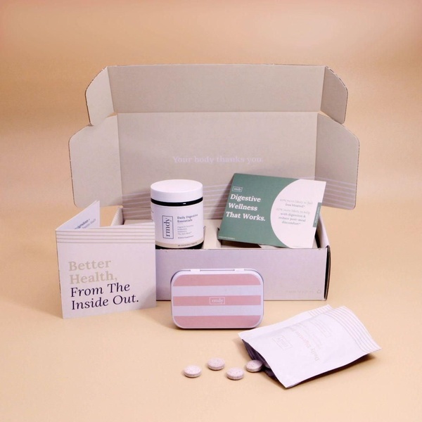 A crisp, high-end product hero shot featuring the digestive supplement packaging, open kit components, and loose tablets on a neutral background.